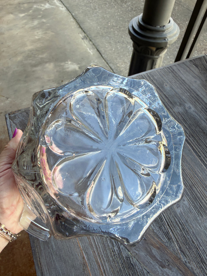 Clear glass object with floral design held by a hand on a textured surface