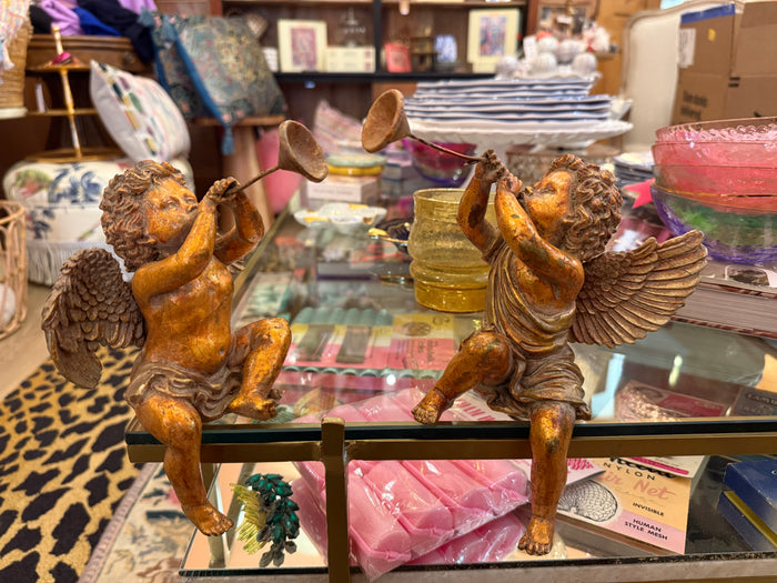 Two angel figurines with trumpets on a glass table in a store setting.