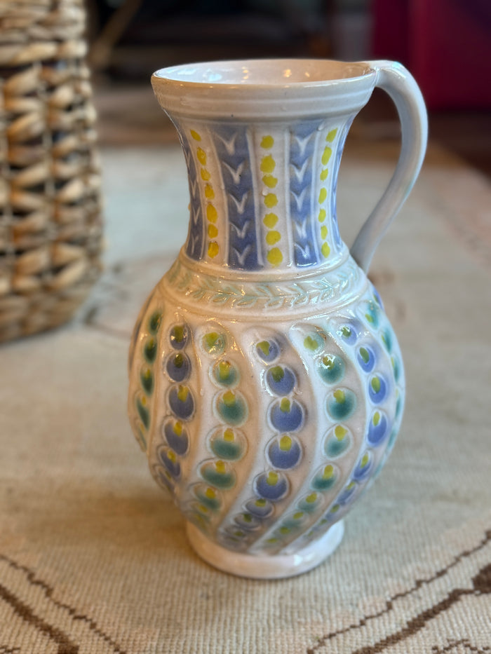 Decorative ceramic pitcher with colorful patterns on a textured surface