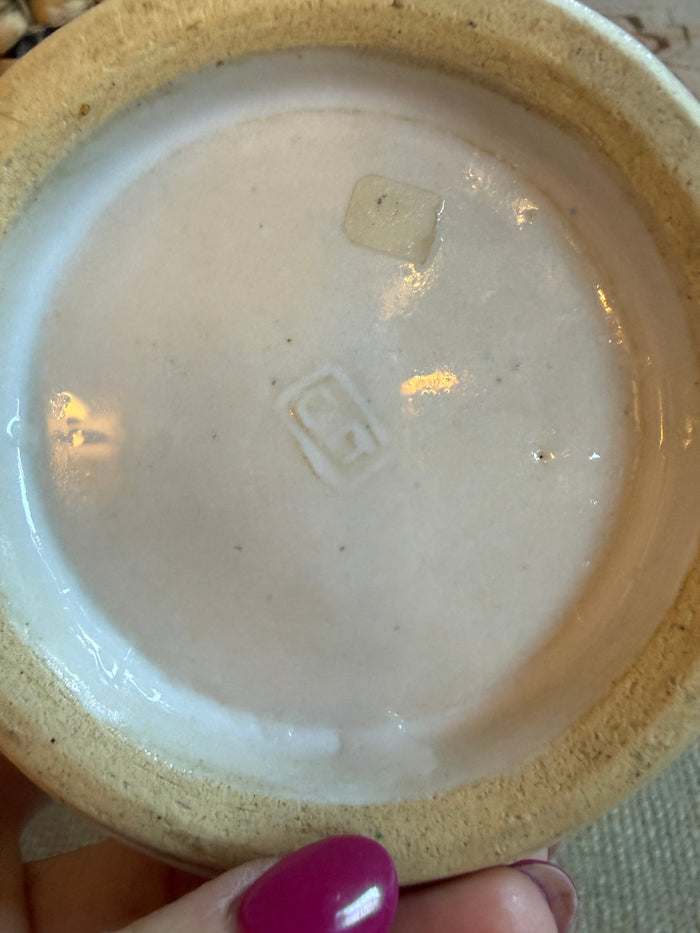 Close-up of a ceramic product with a logo on the bottom, held by a hand.