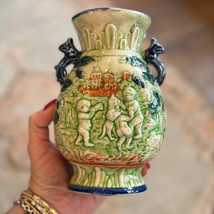 Hand holding a decorative ceramic vase with intricate designs.