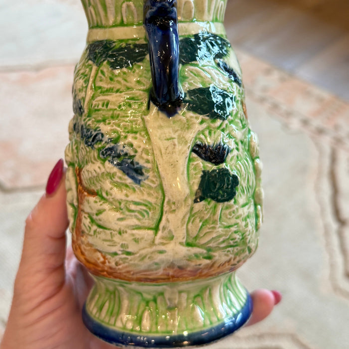 Ceramic mug with green and beige design held by a hand
