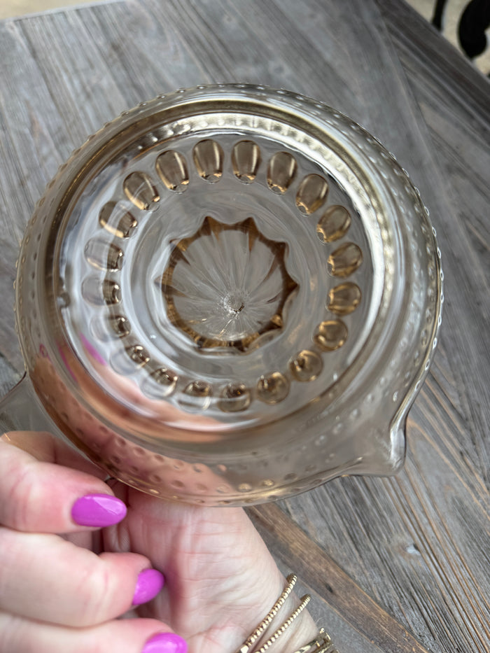 Close-up of a decorative glass item held by a hand with purple nail polish on a wooden surface.