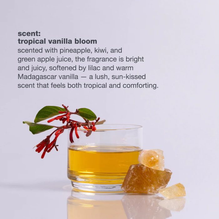 Glass of yellow liquid with a tropical vanilla bloom and ginger root on a light gray background