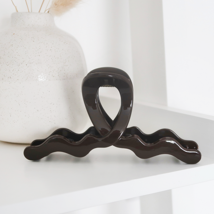 Chocolate brown wavy claw clip by Coconut Lane on a white shelf beside a speckled white vase.