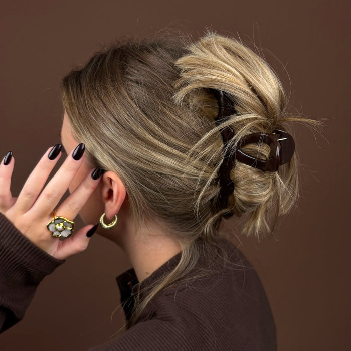 Blonde woman wearing a chocolate brown Coconut Lane wavy claw clip, brown top, gold hoops, and a floral ring.