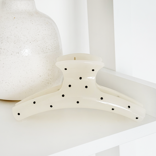 White polka dot claw clip on a white shelf next to a speckled white vase.